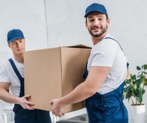 two-handsome-movers-transporting-cardboard-box-in-apartment-e1620131893815.jpg